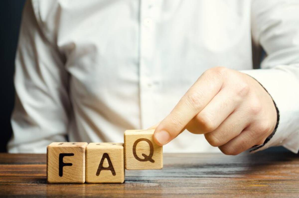 A person in a white shirt adjusts wooden blocks spelling FAQ on a table, symbolizing frequently asked questions.