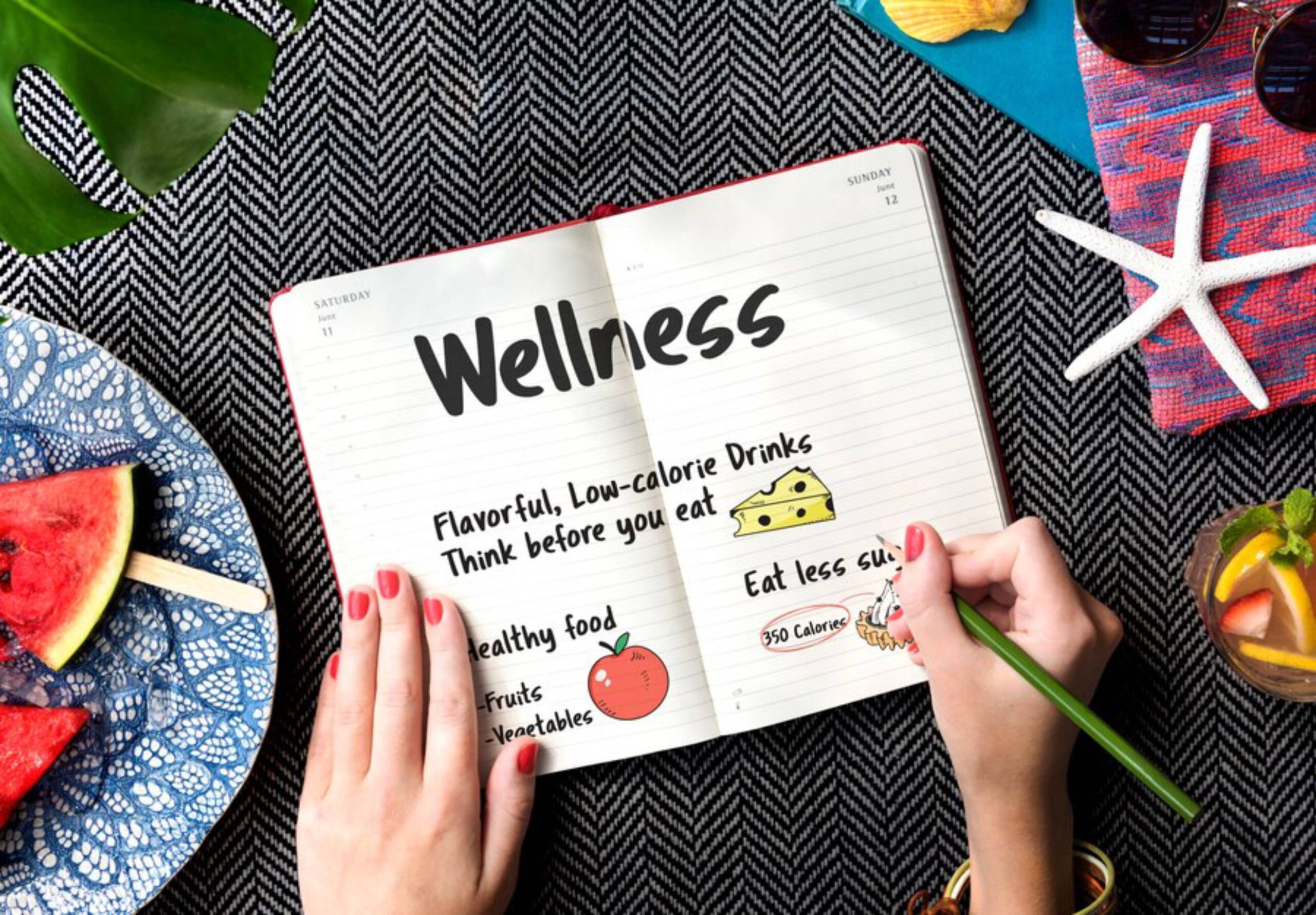 A hand holds a green pen over a notebook titled Wellness, with healthy food tips, alongside fruit and a refreshing drink.