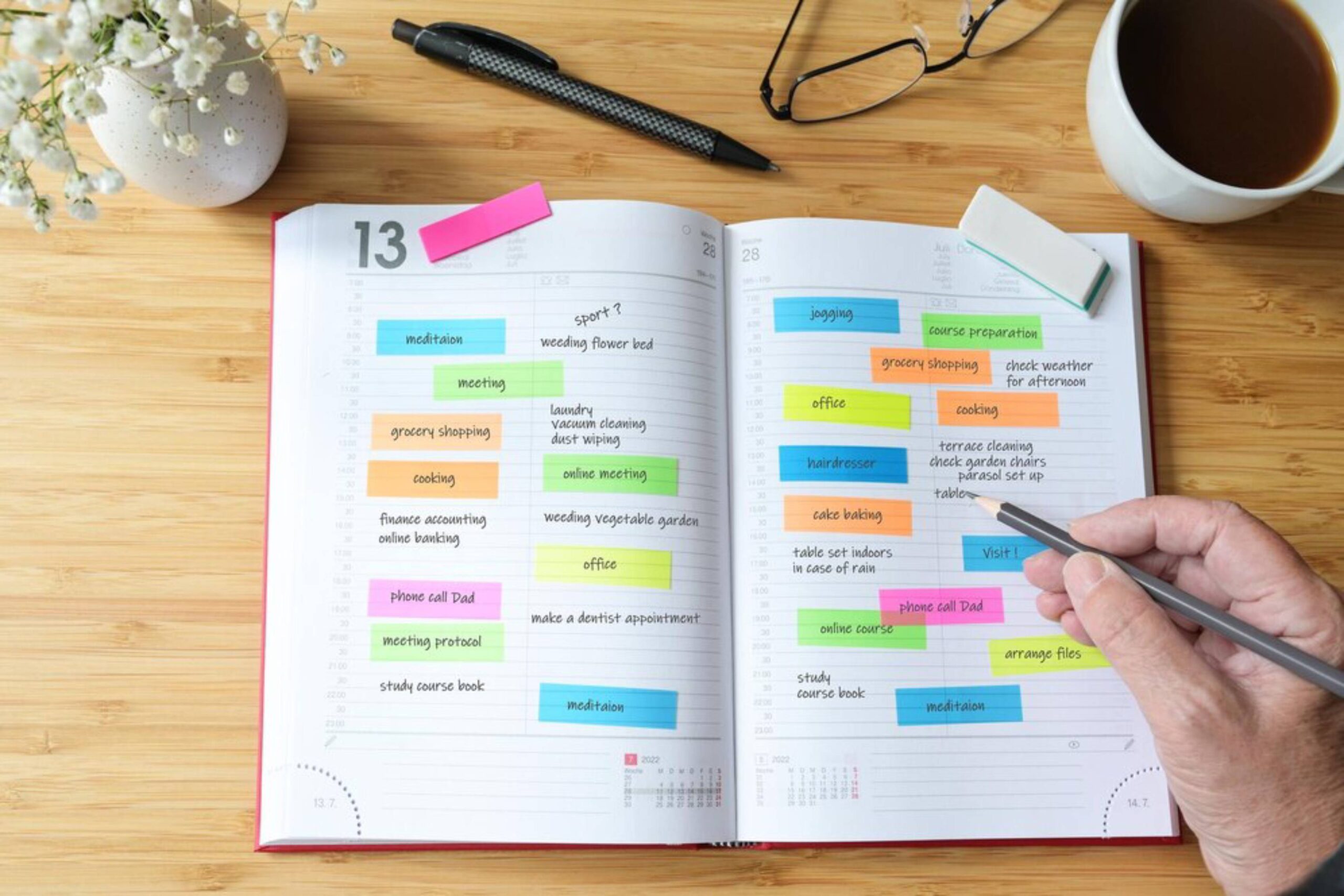 Open planner displaying a variety of colorful notes for tasks, with a hand holding a pencil, a cup of coffee, and glasses nearby.