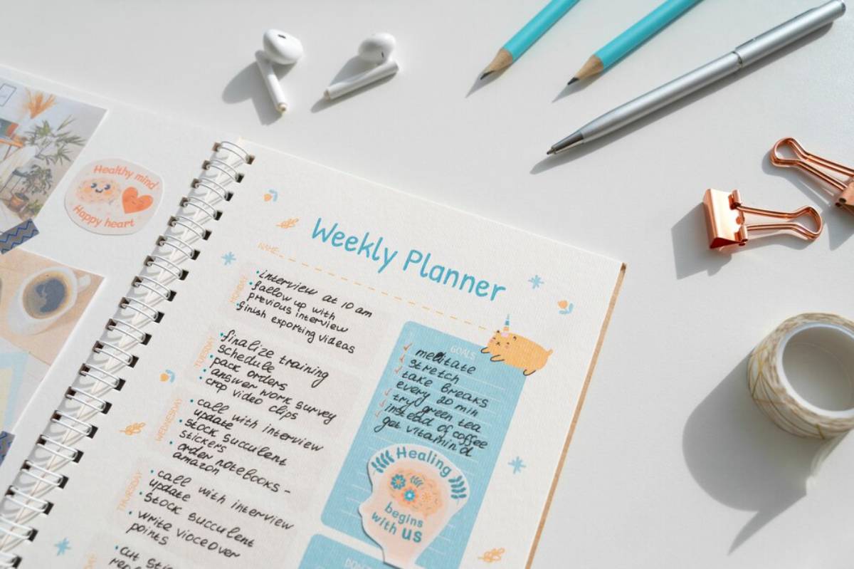 A flat lay of a colorful weekly planner with tasks and goals, surrounded by stationery, earbuds, and decorative elements.