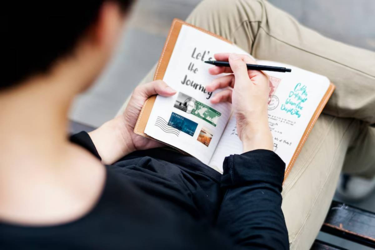 A person writes in a travel journal adorned with photos and stamps, expressing a spirit of adventure and exploration.