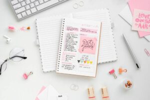 A styled workspace featuring a planner with motivational notes, glasses, a keyboard, and stationery items on a clean desk.