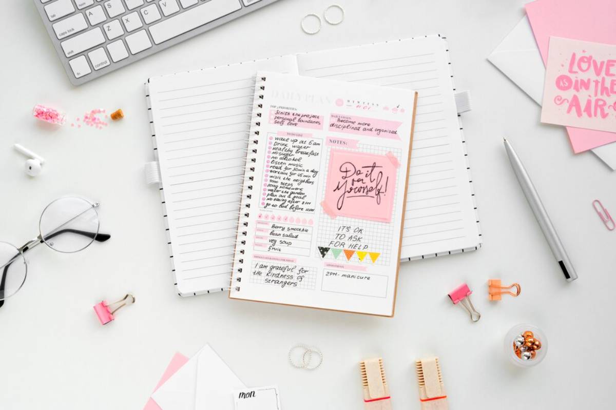 A styled workspace featuring a planner with motivational notes, glasses, a keyboard, and stationery items on a clean desk.